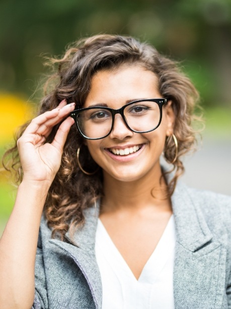 Woman with curly hair smiling and adjusting her glasses