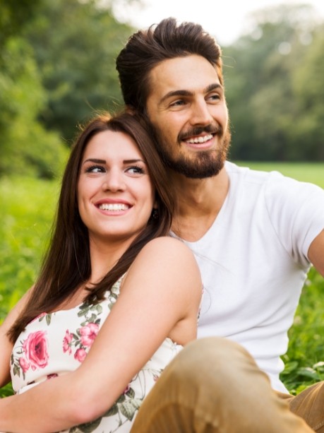 Smiling man and woman sitting in grassy field after cosmetic dentistry in Gorham