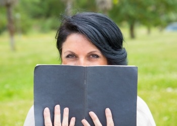 Woman sitting outdoors reading book with black cover