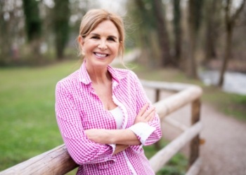 Woman in pink blouse standing on a wooden bridge and smiling
