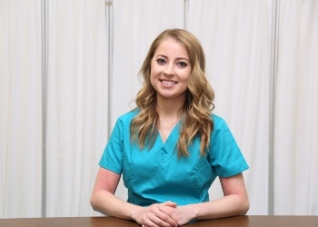 Woman in turquoise scrubs smiling and sitting at desk