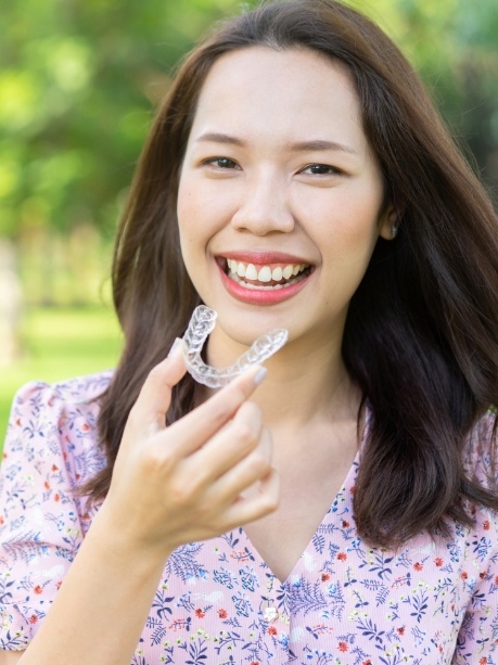Smiling woman holding an Invisalign clear aligner outdoors