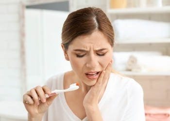 Woman holding bloody toothbrush and touching her cheek in pain