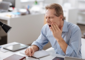 Man sitting at desk and holding his jaw in pain