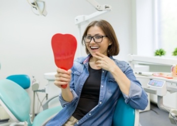 Young woman in dental chair looking at her smile in a hand mirror