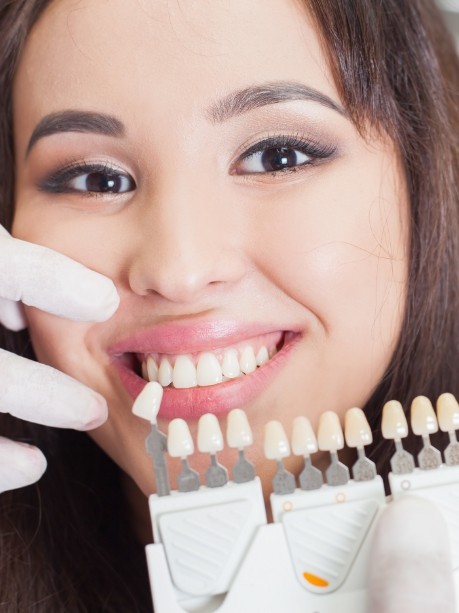 Young woman smiling while dentist holds row of veneers in Gorham