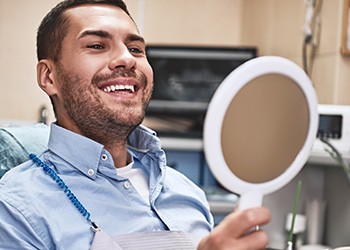 a man looking in a handheld mirror at his teeth