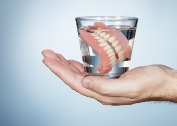 Hand holding a glass of water with soaking dentures