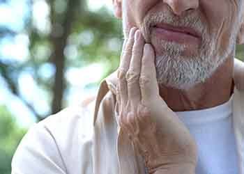 Man with beard rubbing jaw in pain